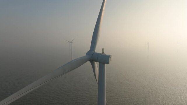 Aerial drone view of offshore wind turbines in the sea covered in thick fog. Industrial wind farm generators in misty ocean water. Concept of renewable energy, foggy weather and green power.