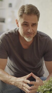 Older man at home, sitting on couch in white living room. Portrait of happy, mature age, middle age, mid adult man in 50s, smiling.
