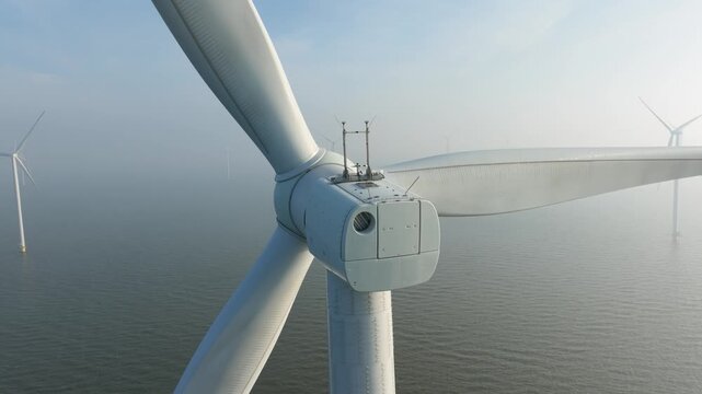 Aerial drone view of offshore wind turbines in the sea covered in thick fog. Industrial wind farm generators in misty ocean water. Concept of renewable energy, foggy weather and green power.