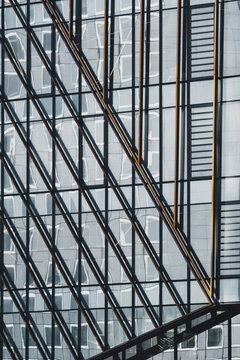a diagonal escalator rises inside glass architecture, crossing the facade as reflection, windows, urban structure and geometric grid tighten the frame.