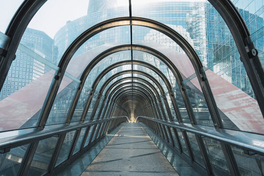 a glass tunnel carries urban architecture into a curved walkway, where reflection, perspective, structure, passage and symmetry pull the eye forward.