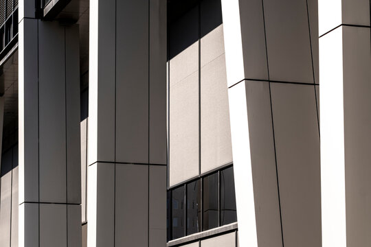 sharp shadow falls through urban architecture, cutting the facade between panels, cladding, windows and exterior structure into geometric rhythm.