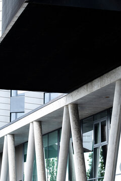 concrete columns cut through urban architecture below a dark overhang, while geometric shadow sharpens the facade and exterior structure.