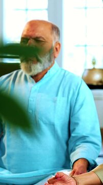 Indian senior couple doing omkar pranayama or yoga at home in the morning sitting with folded legs in modern living room chanting aum, practicing mindful breathing exercise for health