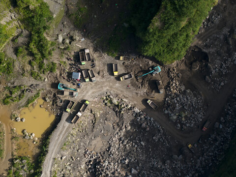 Aerial view of Tambang Pasir Merapi Kali Gendol Sand Mine with excavators loading trucks on a rocky terrain surrounded by lush greenery Kecamatan Cangkringan, Daerah Istimewa Yogya, Indonesia.
