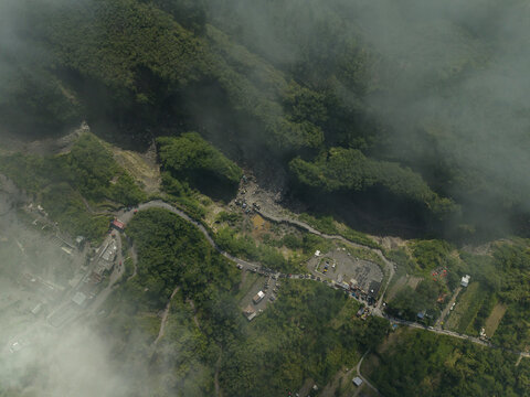 Aerial view of Tambang Pasir Merapi Kali Gendol Sand Mine with winding roads, lush green forests, and misty clouds in Kecamatan Cangkringan, Daerah Istimewa Yogya, Indonesia.
