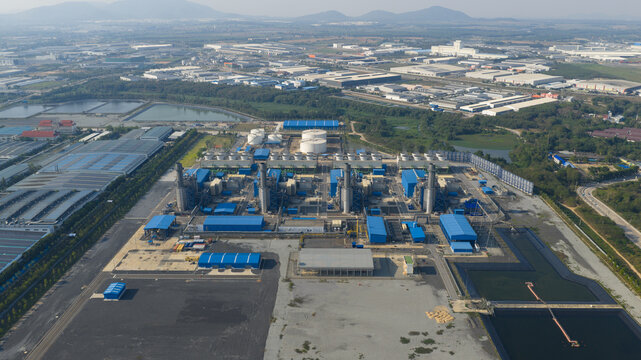 Aerial view of a large industrial power plant complex with blue buildings, cooling towers, and storage tanks in Map Yang Phon, Rayong, Thailand.
