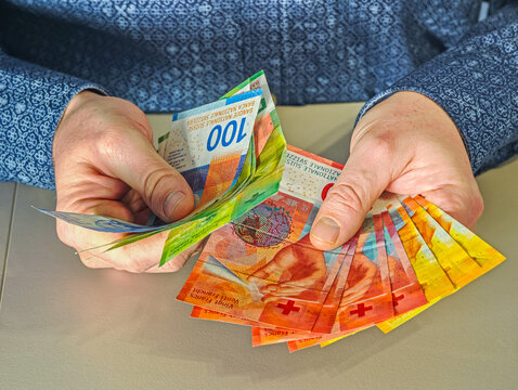 Man holding colorful 10, 20, 50 and 100 Swiss Francs bills planning travel budget or shopping trip