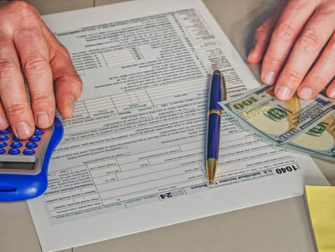 US Individual Income Tax Return form 1040 with hundred dollar bills, pen and blue calculator