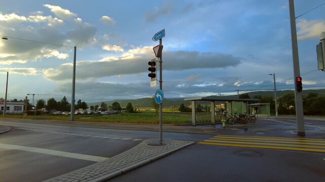 Empty road intersection with traffic lights and a bus stop under a cloudy sky