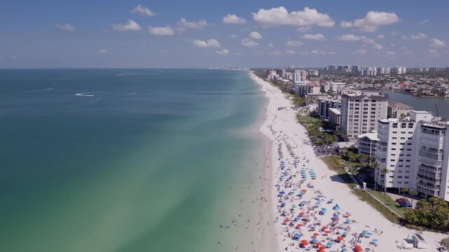 Aerial drone view traveling along busy Naples, Florida coastline and beach