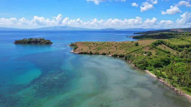 Aerial drone footage of Ketapang beach edge, with Gili Dewa island, with white sand, coral reef and pristine blue water, in sunny weather, in Sumbawa regency, Sumbawa island, Indonesia 