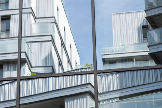 metal facade and glass balcony lines define residential windows beside urban architecture, where exterior reflection meets a soft blue sky