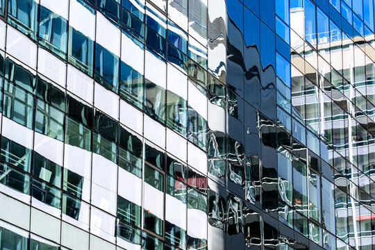 glass facade reflection bends office windows across urban architecture, creating a blue pattern on an exterior wall of layered mirrored surfaces