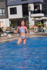 Naklejka premium A joyful candid shot of a smiling young girl playing in a crystal-clear blue swimming pool at a modern resort.