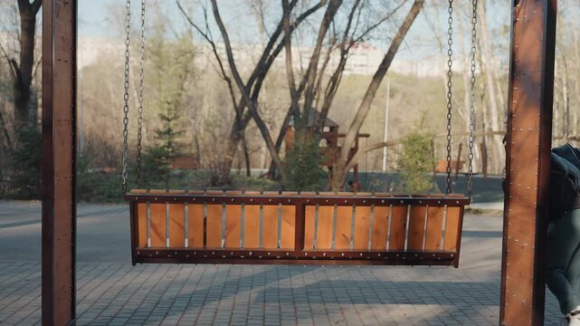 Park planter swing wooden bench prowler edges into frame, crouches behind planter, glances around, reaches under bench to snatch unseen item, hasty retreat across paved plaza, crisp daylight, bare