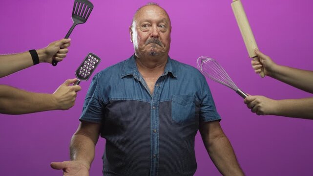 Man surrounded by hands holding whisk, spatula, grater and rolling pin, making a surprised face in a studio; bemusement.