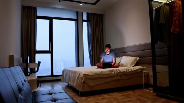 Happy woman using a laptop computer sitting on her bed at night