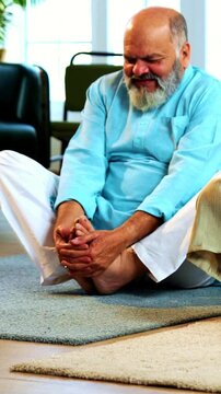 Indian senior couple doing stretching doing butterfly warmup or yoga at home in the morning performing sukshma yogic kriya for hip joints while sitting on mat in modern living room