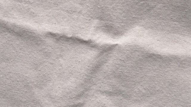 Wrinkled natural linen fabric texture in neutral beige color. Closeup textile background with soft folds. Organic woven material. Abstract crumpled canvas surface. Rotation. Top view
