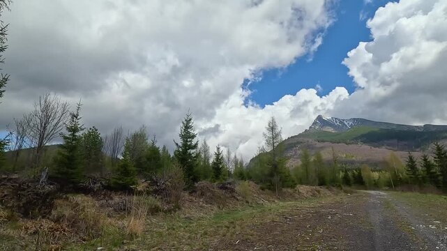Panoramic view of a dirt road leading towards a mountain peak on a partly cloudy day