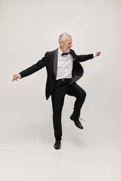 Dancing in elegance, a bearded man in a tuxedo shows charm in a serene grey studio