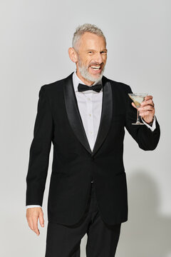 Handsome middle aged man in tuxedo holding a cocktail in a stylish grey studio setting