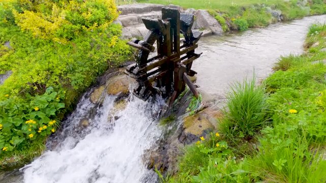 Small wooden water wheel rotating from the flow of a stream in a lush green mountain landscape
