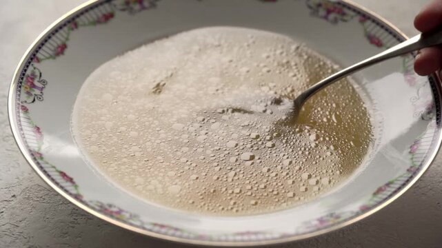 Person's hand stirring bone broth or soup in a plate with a spoon, closeup