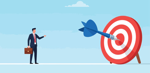 Businessman pointing at giant dart hitting center of target bullseye representing achievement of goals success high performance and strategic hit accurate. © sjeixh