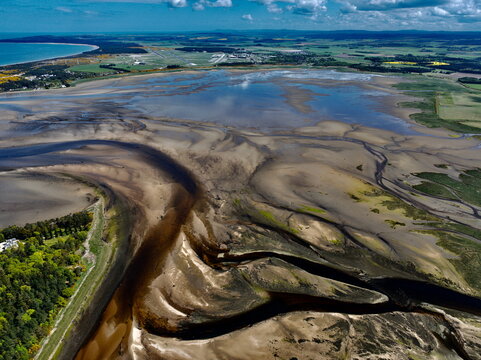 Aerial view of the intricate tidal patterns and winding water channels of Findhorn Bay surrounded by green fields and the coastline in Findhorn, Scotland, United Kingdom.