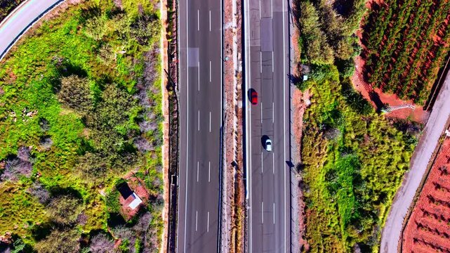 Aerial shot of vehicles driving on a divided road between green and red terrain. Straight top down view of a multi lane highway.