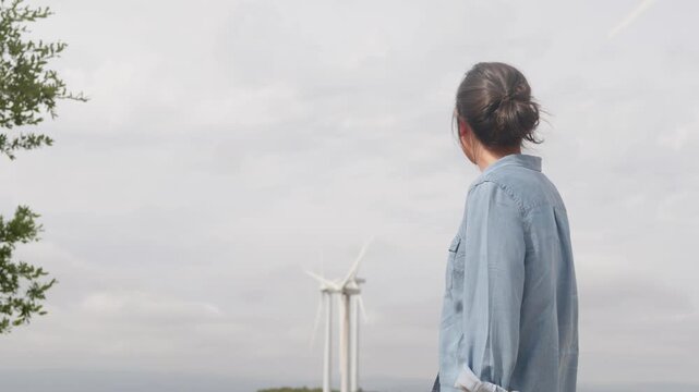 Female engineer observing rotating wind turbines at a renewable energy farm, showcasing sustainable power generation and environmental conservation for a greener future