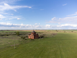 Obraz premium Abandoned red brick church with domed roof and cross sits in a green field