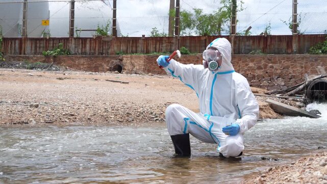 Scientists wearing PE chemical protective suits stand on drainage pipes to collect water samples and debris, including dead fish, to check water quality after wastewater treatment and chemical polluta