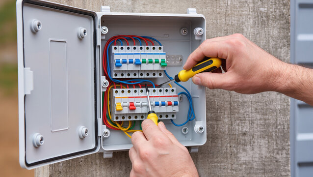 Electrician repairing outdoor electrical breaker panel.
Professional technician installing external power box.
Technician maintaining electrical system with tools.
Hands of electrician at work 