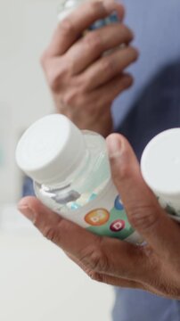 Vertical close up shot of anonymous man holding multiple medication bottles in hand and reading labels while choosing multivitamins for matures