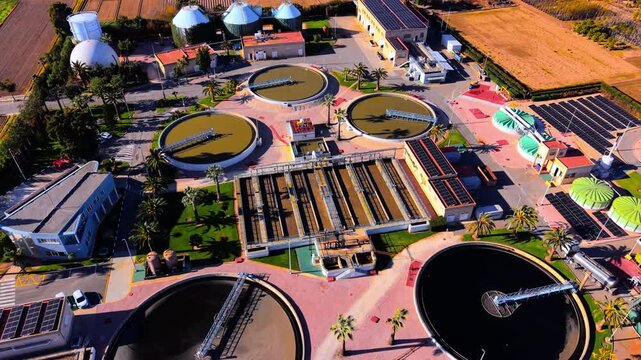 Technical sewage treatment station featuring circular clarifiers, solar panels, and water filtration infrastructure. Wastewater treatment plant facility with purification tanks.