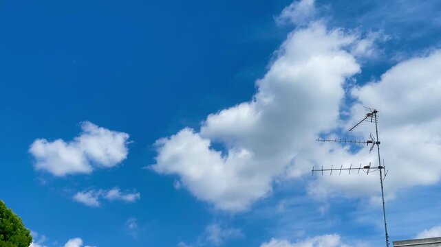 Sky and Antenna: A clear blue sky is punctuated by fluffy, white clouds and a television antenna. A sense of openness and communication.