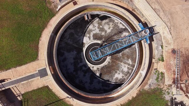 Top-down aerial view of an empty circular clarifier tank at a wastewater treatment facility, showing the central rotating mechanism and scraper bridge during maintenance