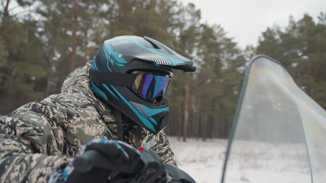 Closeup atv helmet reflection snowy forest mirrored visor reflecting pine landscape rider adjusting strap camouflage jacket texture visible windshield edge quiet anticipation before acceleration