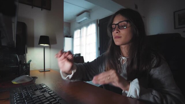 Video of a young woman sitting at her computer desk at home and starting a work video call. Hybrid work and remote communication concept.
