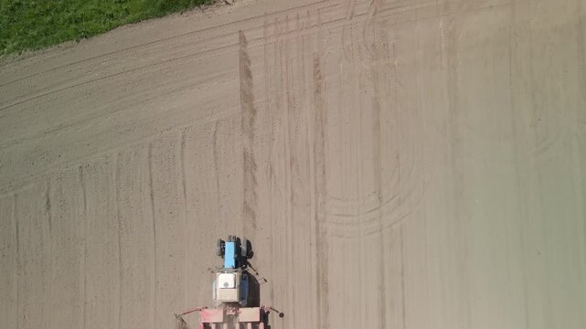 Top down aerial view of a tractor sowing seeds in a field. Vertical bird's eye view of agricultural machinery planting crops. Geometric patterns of soil cultivation in spring agribusiness.