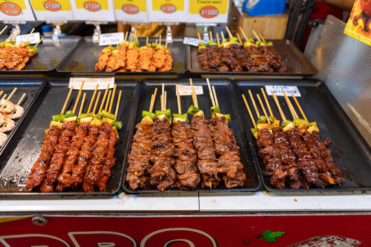 bustling night market in Bangkok, colorful street food stalls serving sizzling skewers, people enjoying authentic Thai cuisine