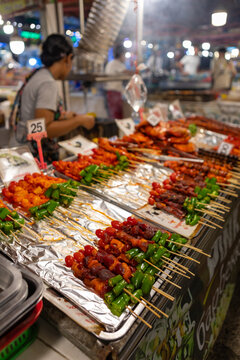 bustling night market in Bangkok, colorful street food stalls serving sizzling skewers, people enjoying authentic Thai cuisine
