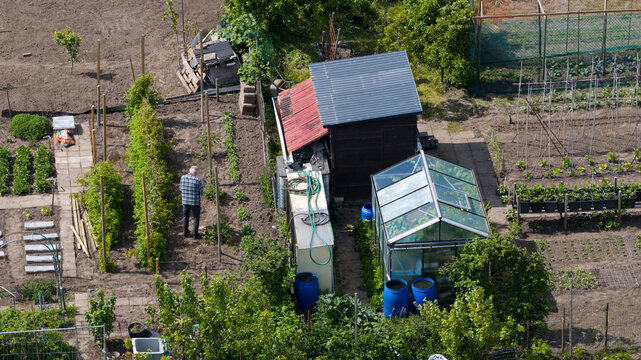 Aerial view of Amateur Gardeners Association Het Kloosterpark with a man working near a greenhouse and garden beds in De Bilt, Utrecht, Netherlands.