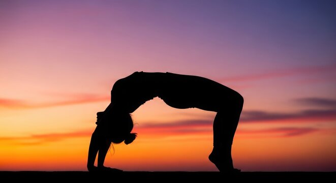 Silhouette of woman performing backbend yoga pose at sunset