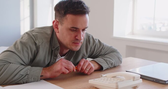 Man waiting for landline phone call at work in office workplace. Person in anxiety, stress and disappointment from late calling and silence, employee sitting at desk by window and training patience