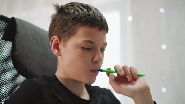 White grandson thoughtful pause with green pen, closeup portrait in mesh chair by window, quiet reflective expression, soft light and bokeh, teen coping habit and introspective mood