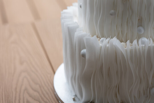 Close up of modern wedding cake decorated with edible wafer paper and sugar pearls. Elegant minimalist white dessert with luxurious appearance.
